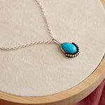 Load image into Gallery viewer, Necklace with a turquoise pendant on a wooden stand with a pink fabric background

