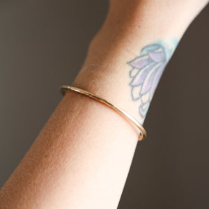 Brass bracelet on a wrist with a tattoo of a flower.